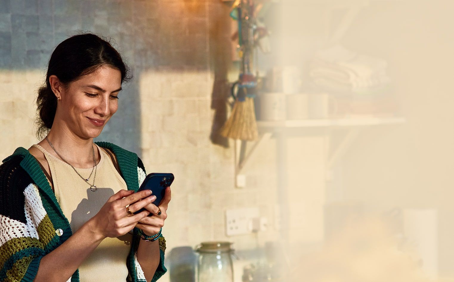 A woman smiles at her phone in a sunlit kitchen